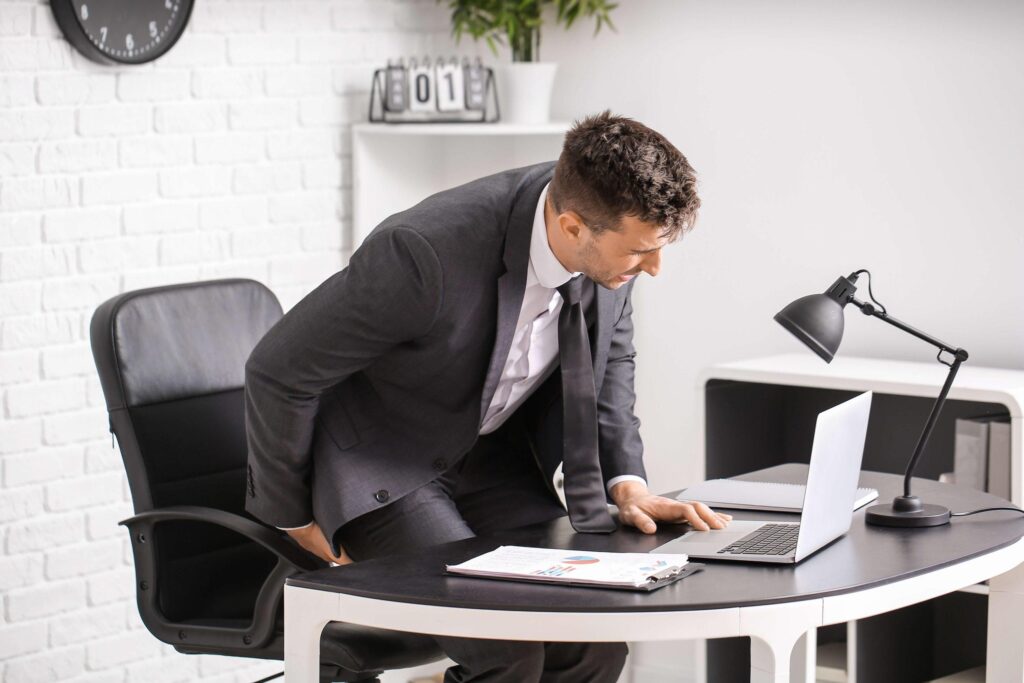 Mann im Büro mit Fehler beim Sitzen und unteren Rückenschmerzen
