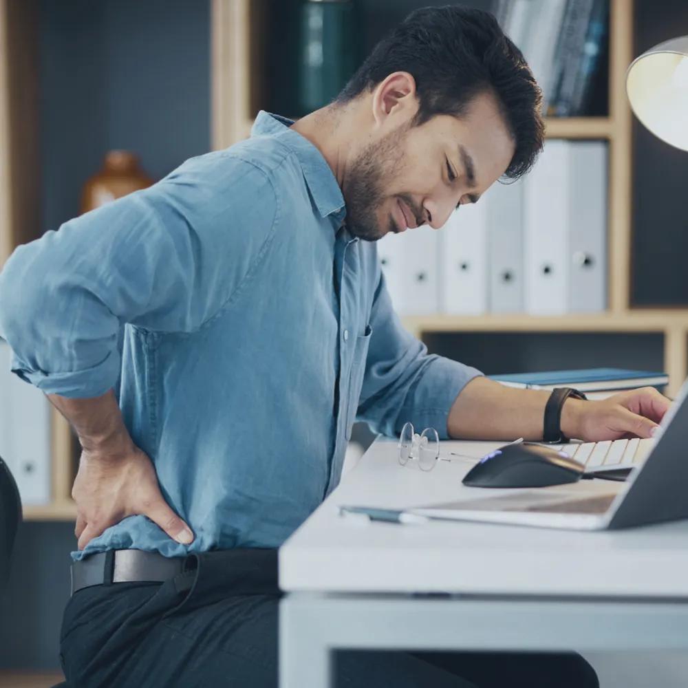 Mann im Büro mit Fehler beim Sitzen und Schmerzen im unteren Rücken